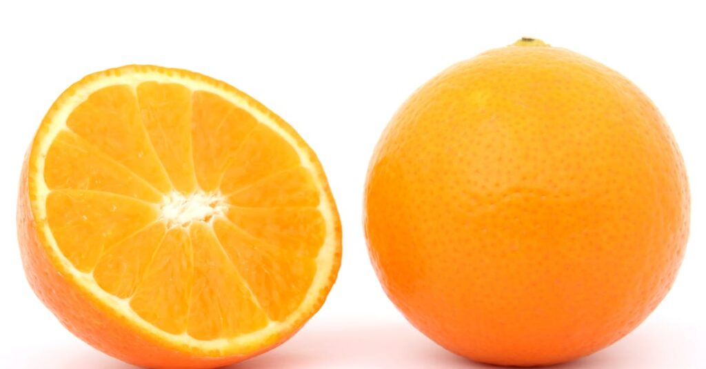 Close-up of a whole orange and a sliced half on white background, highlighting freshness.